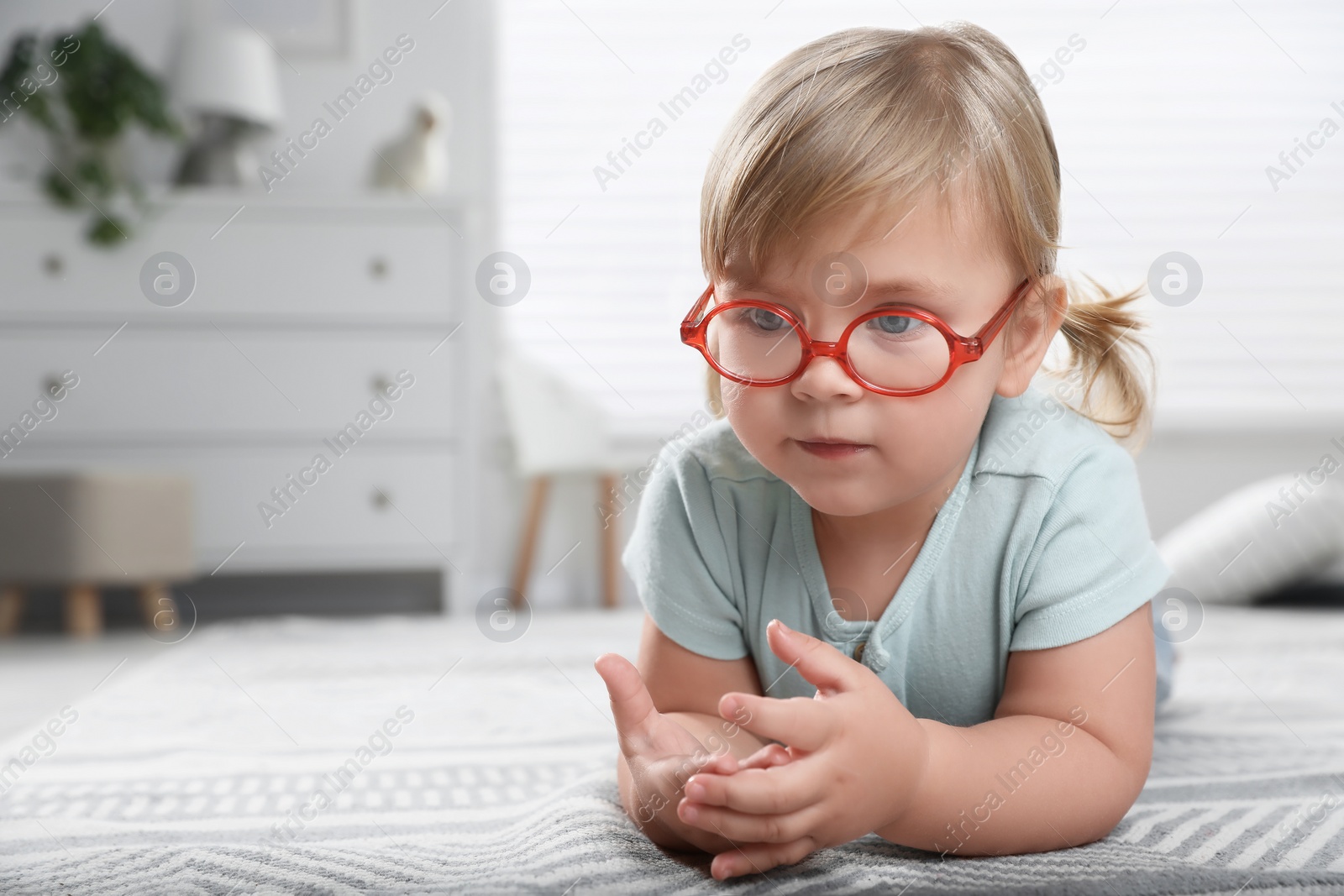 Photo of Cute little girl in glasses on floor at home. Space for text