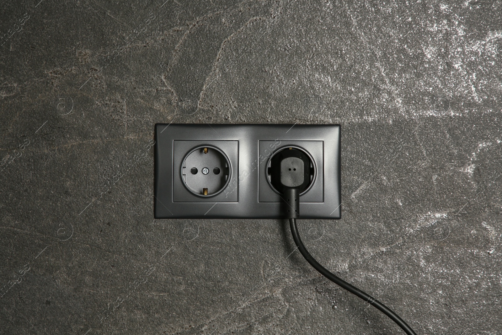 Photo of Power sockets with inserted plug on dark grey wall. Electrical supply