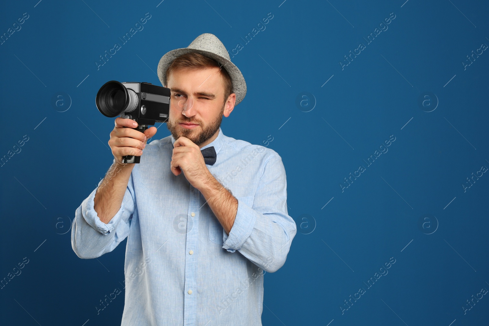 Photo of Young man with vintage video camera on blue background. Space for text
