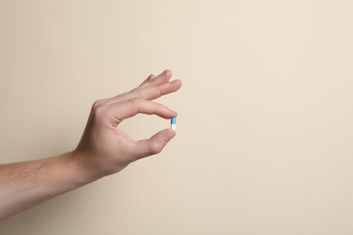 Photo of Man holding pill on beige background, closeup. Space for text