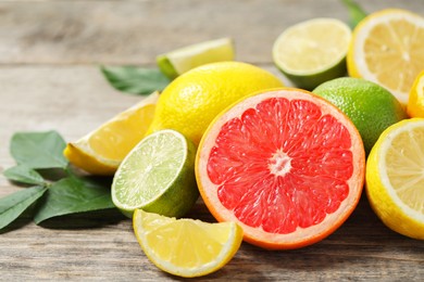 Photo of Different fresh citrus fruits and leaves on wooden table, closeup