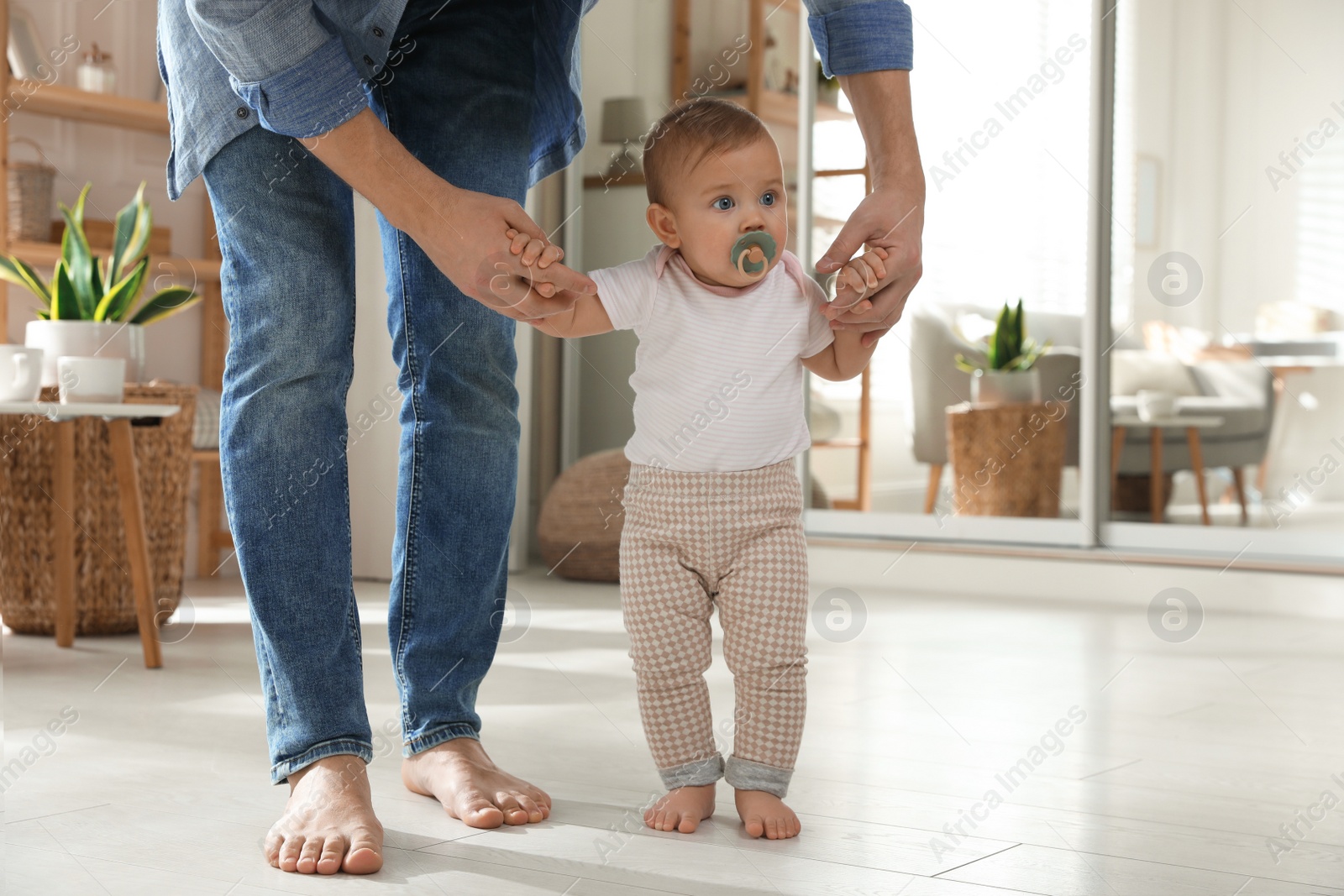 Photo of Father supporting his baby daughter while she learning to walk at home