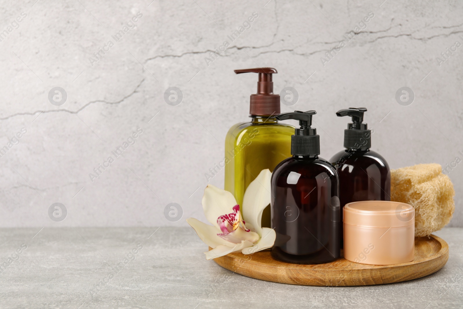 Photo of Shampoo bottles, hair mask, loofah and orchid flower on light grey table, space for text