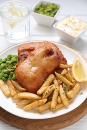 Photo of Tasty fish, chips, sauce, peas and lemon on white wooden table, closeup