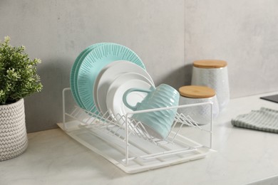 Drainer with different clean dishware and cup on light table indoors