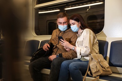 Photo of Couple with mobile phone wearing medical masks in subway train. Public transport