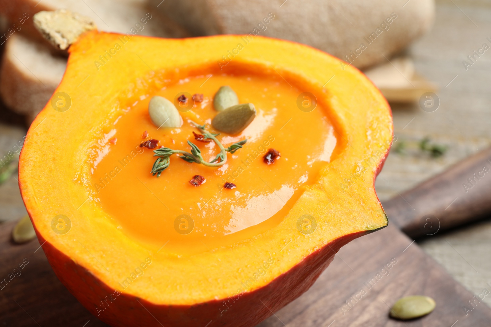 Photo of Tasty cream soup in pumpkin half on board, closeup