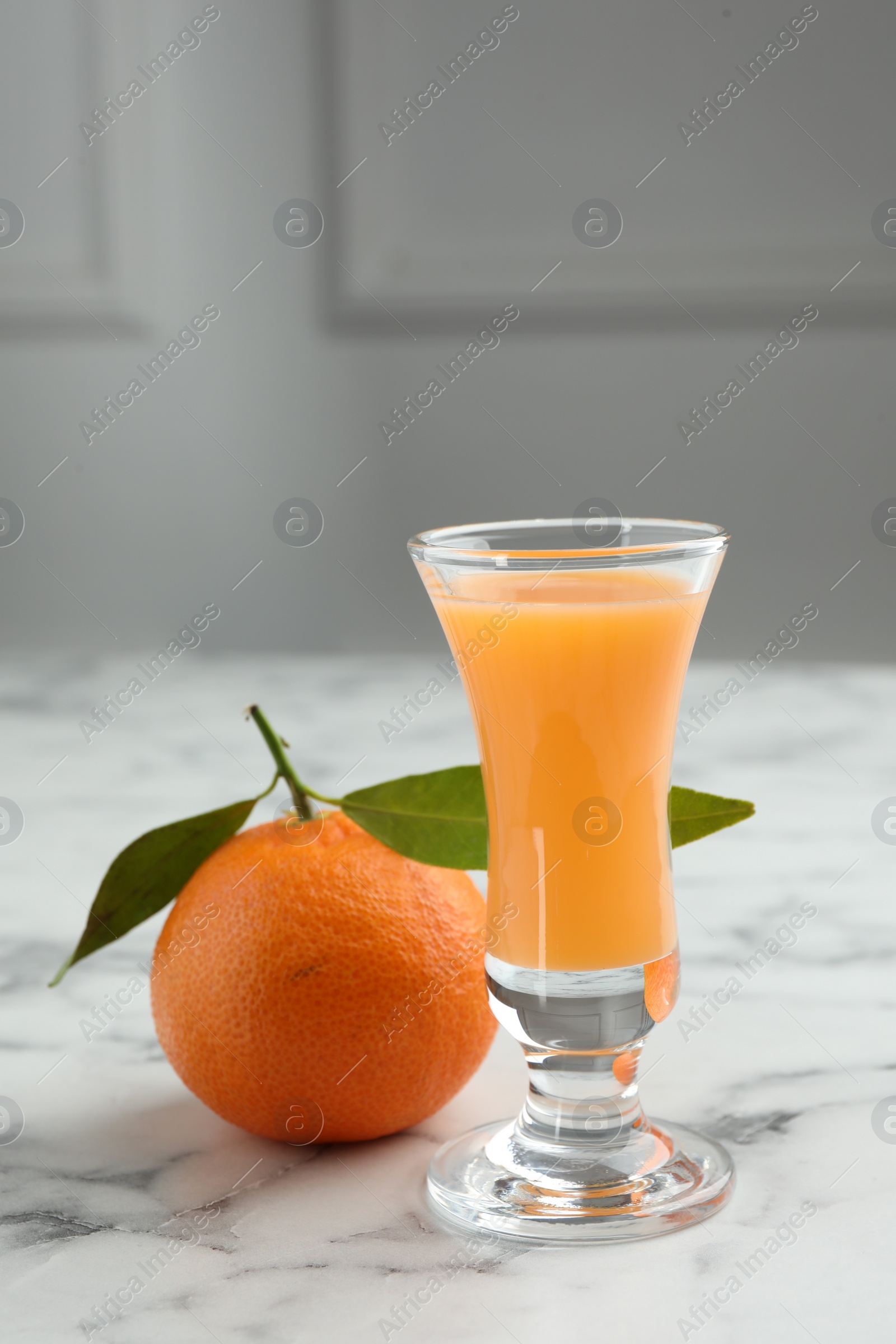 Photo of Delicious tangerine liqueur in shot glass and fresh fruit on white marble table