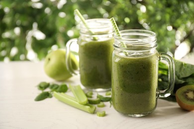 Photo of Delicious green juice and fresh ingredients on white table. Space for text