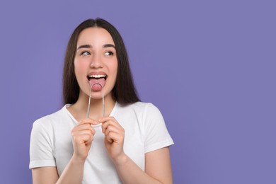 Photo of Happy woman brushing her tongue with cleaner on violet background, space for text