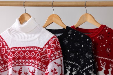 Different Christmas sweaters hanging on rack against light background, closeup