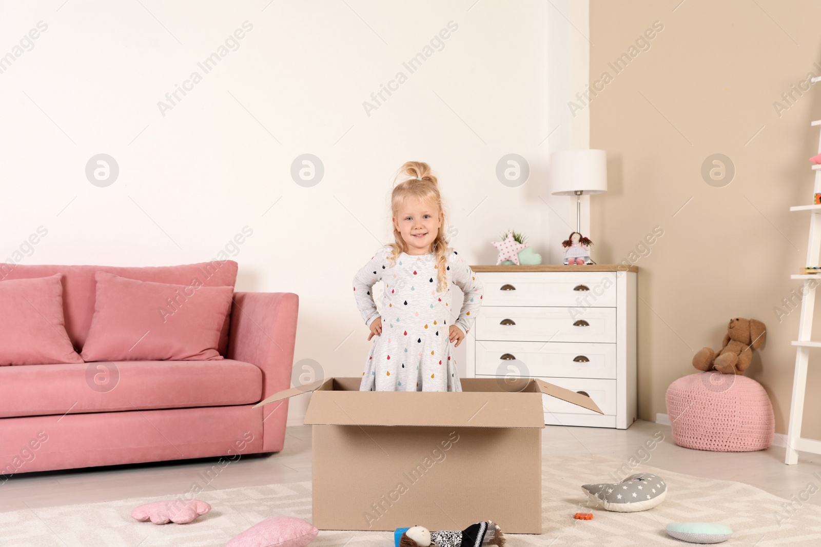 Photo of Cute little girl playing with cardboard box at home