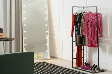 Clothing rack with colorful sequin party dresses and shoes near mirror in boutique, space for text