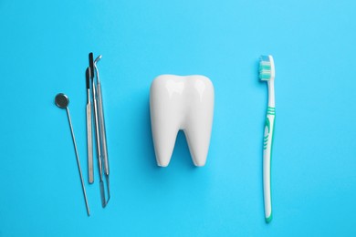 Photo of Tooth shaped holder, brush and dentist's tools on light blue background, flat lay