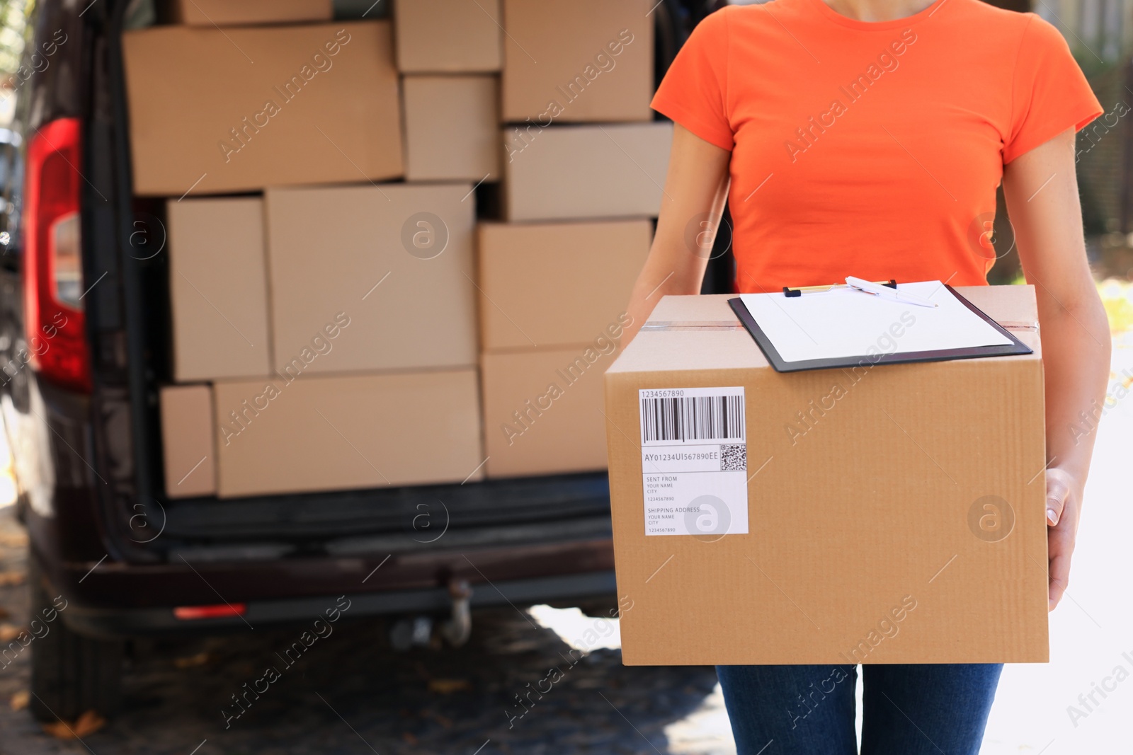 Photo of Courier holding package near delivery truck outdoors, closeup