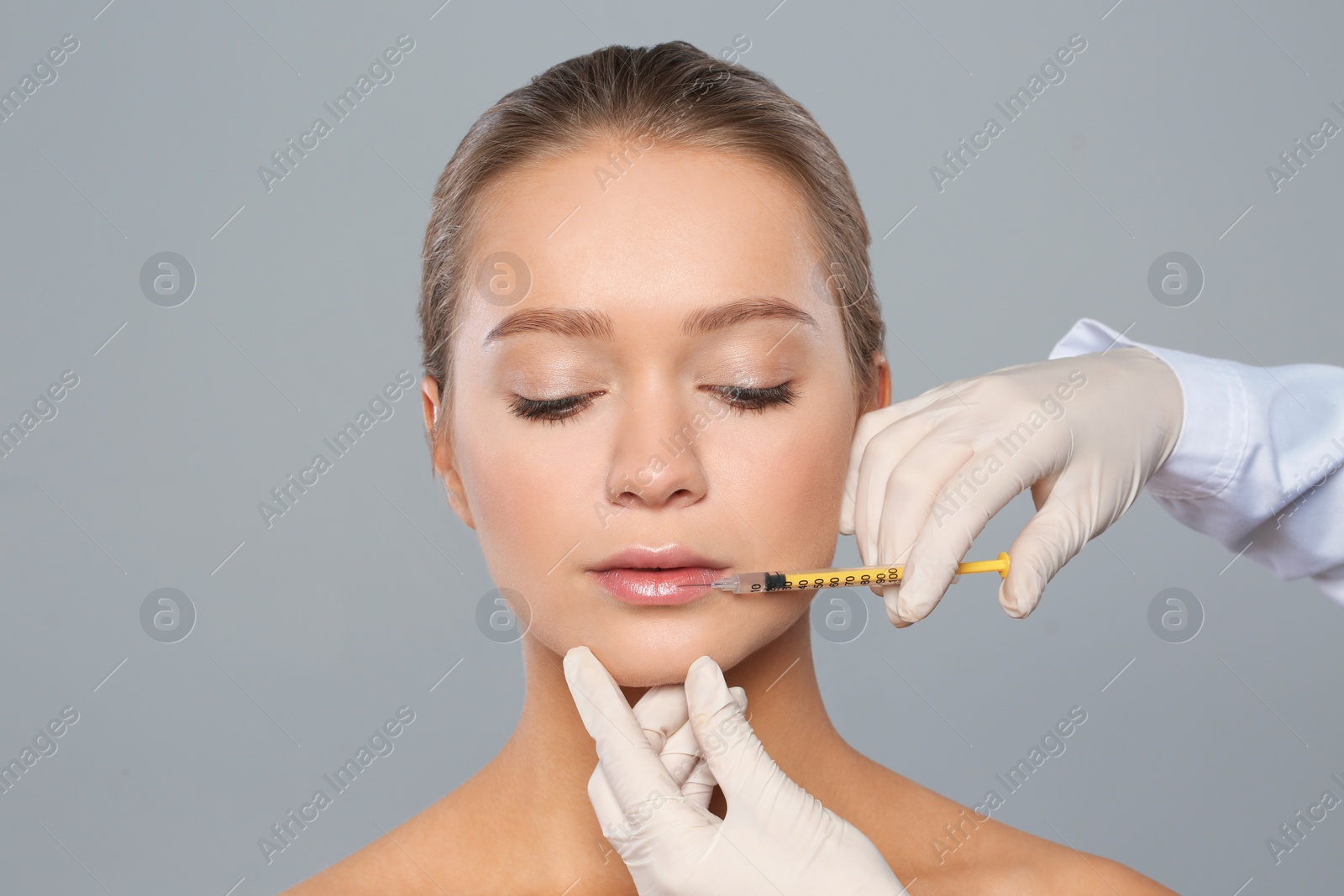 Photo of Young woman getting lips injection on grey background. Cosmetic surgery