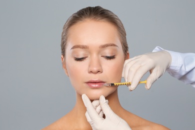 Young woman getting lips injection on grey background. Cosmetic surgery