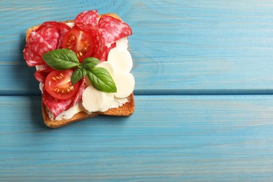 Tasty toast with butter, salami, tomato, cheese and basil on light blue wooden table, top view. Space for text