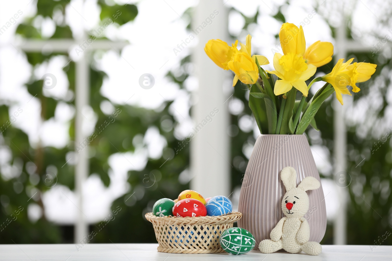 Photo of Festive composition with Easter eggs on table against blurred window, space for text