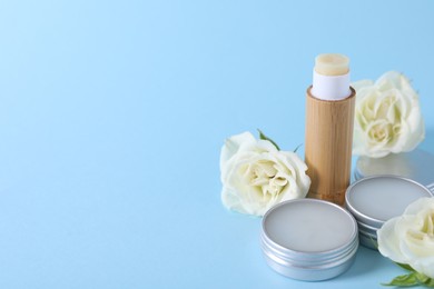 Photo of Different lip balms and rose flowers on light blue background. Space for text