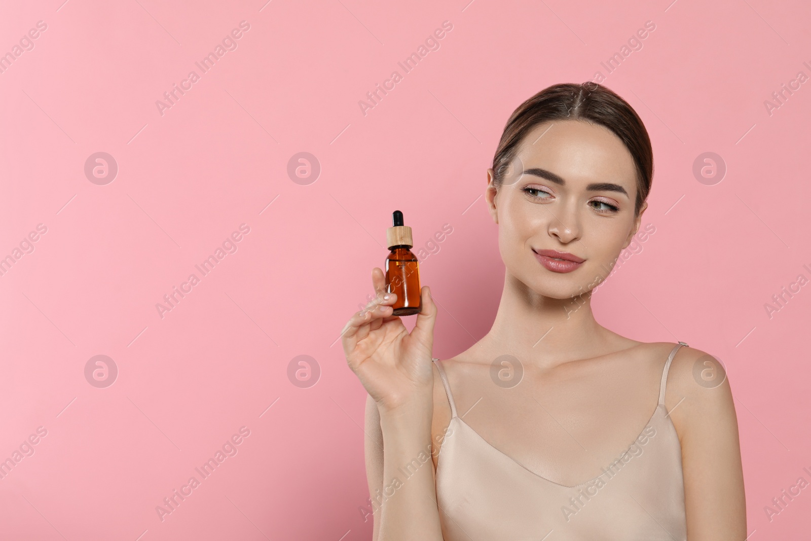 Photo of Young woman with bottle of essential oil on pink background, space for text