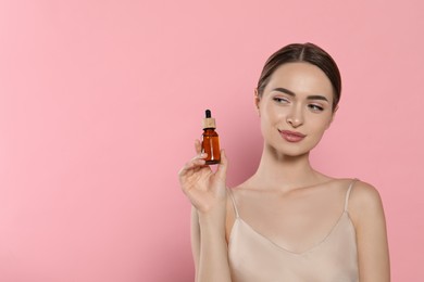 Young woman with bottle of essential oil on pink background, space for text