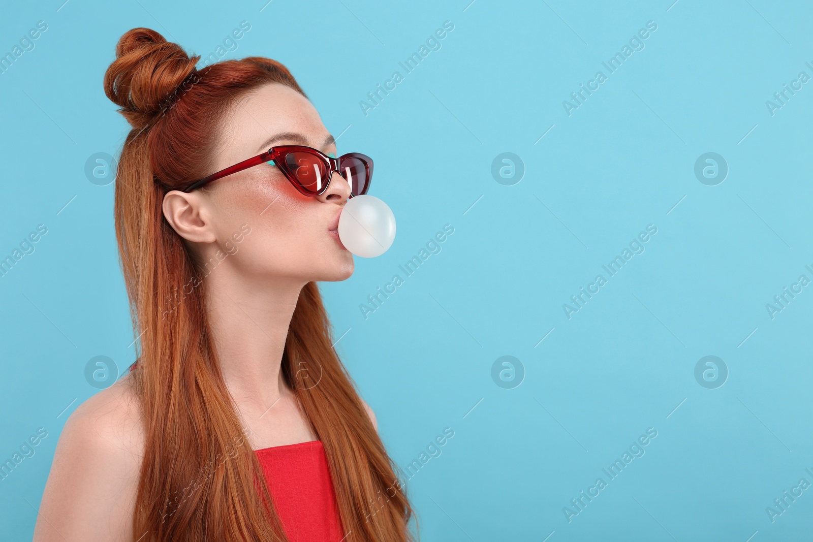 Photo of Beautiful woman in sunglasses blowing bubble gum on light blue background. Space for text