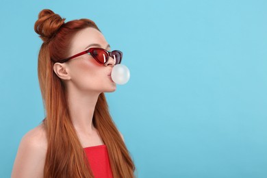 Photo of Beautiful woman in sunglasses blowing bubble gum on light blue background. Space for text