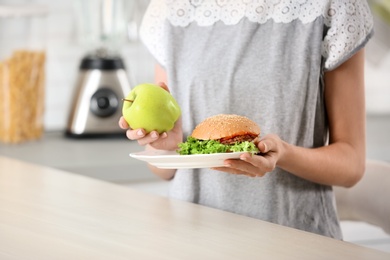 Photo of Woman holding tasty sandwich and fresh apple over table. Choice between diet and unhealthy food
