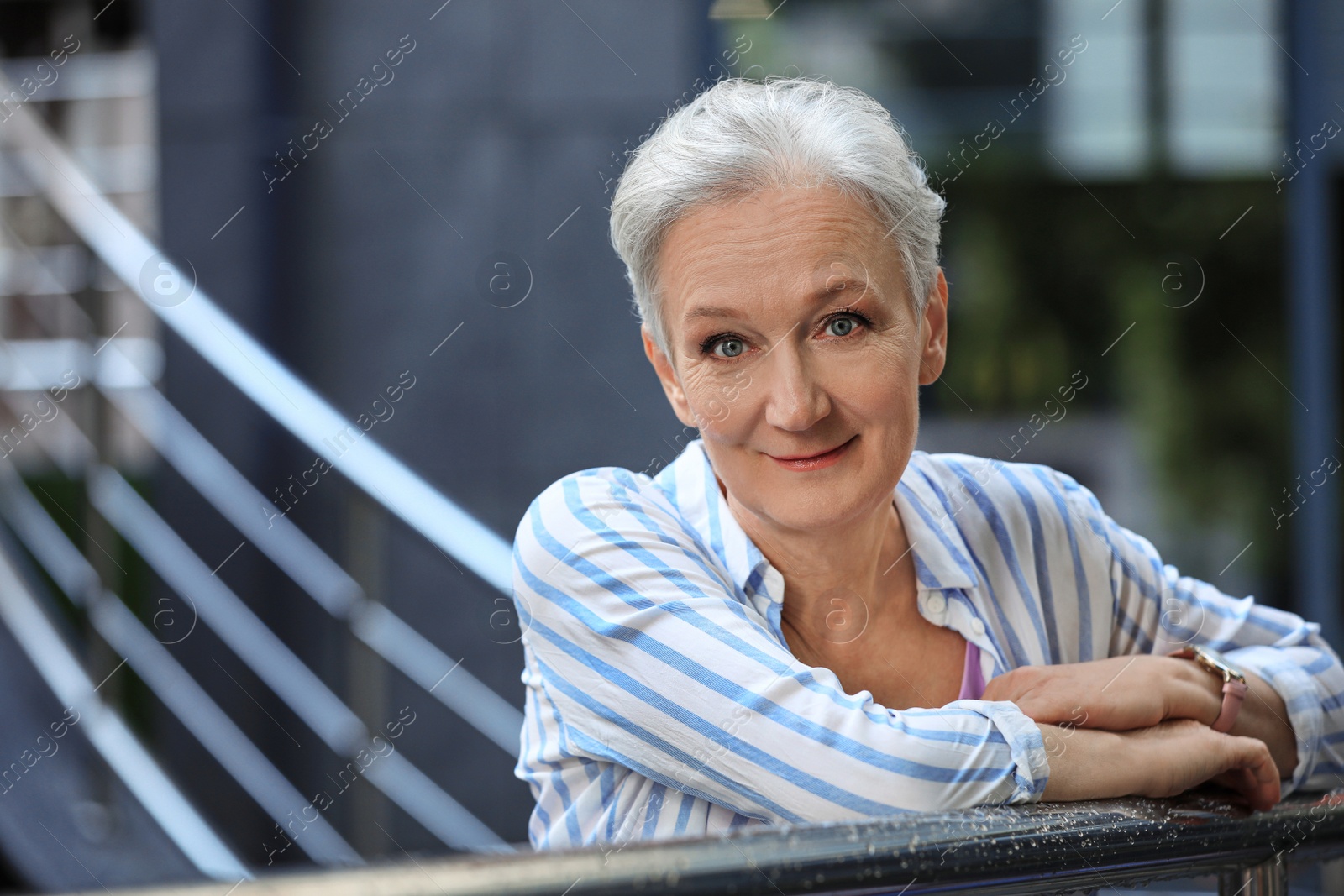 Photo of Happy mature woman near metal handrail on city street, space for text. Smart aging