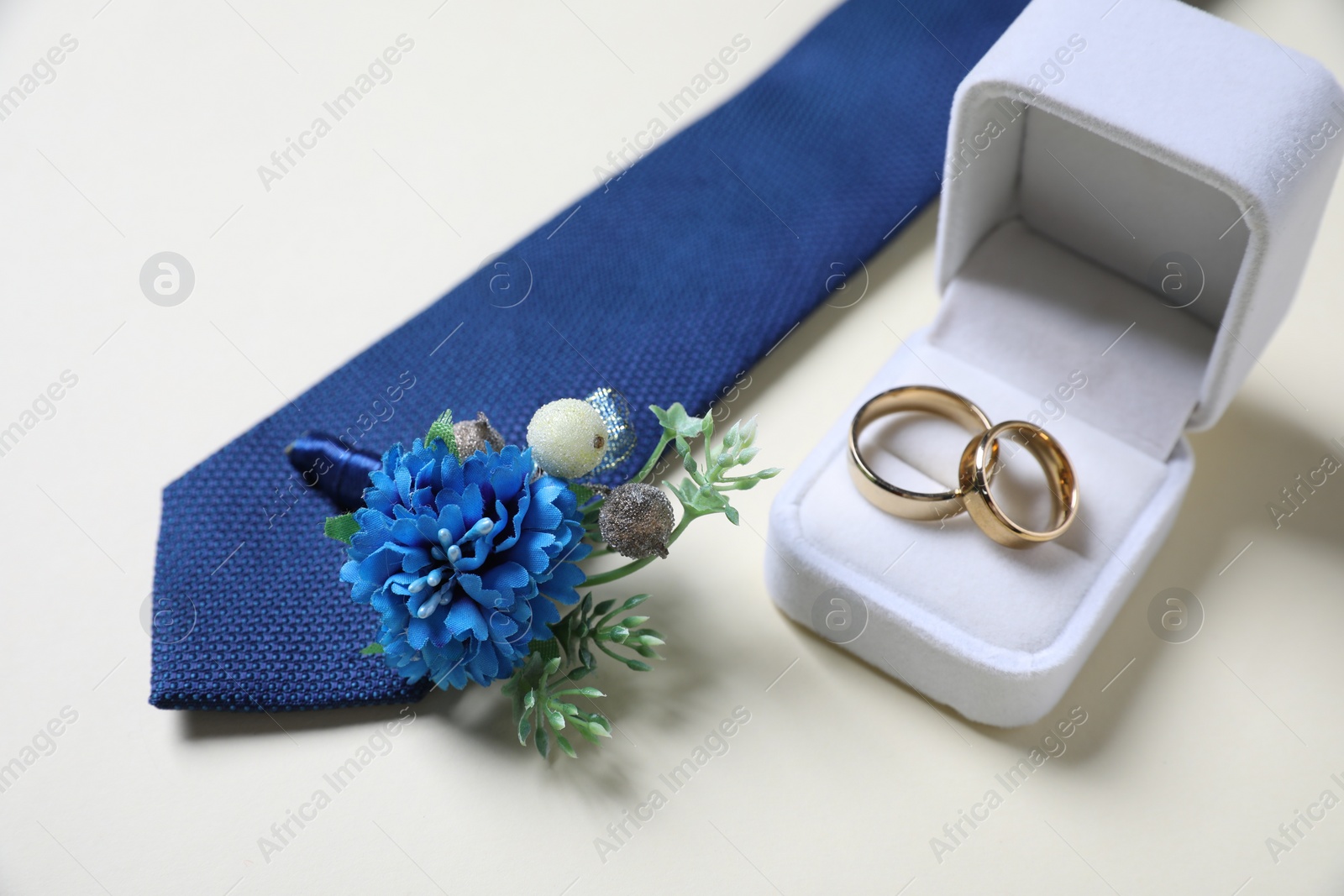 Photo of Wedding stuff. Stylish boutonniere, blue tie and wedding rings on light background, closeup