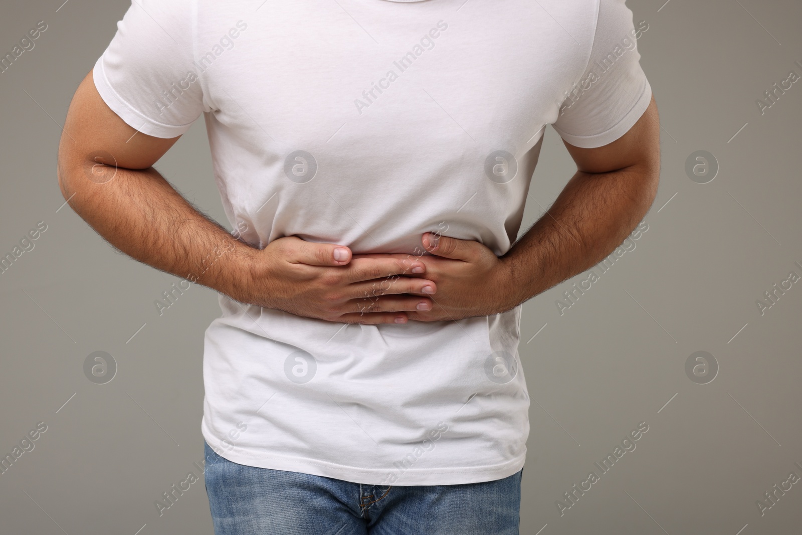 Photo of Young man suffering from stomach pain on light grey background, closeup