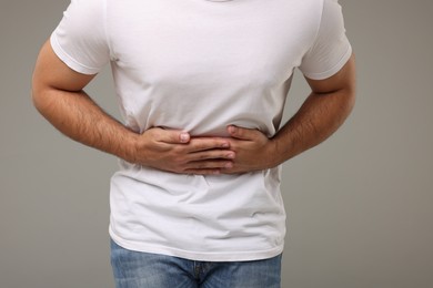 Photo of Young man suffering from stomach pain on light grey background, closeup