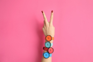 Woman with many bright wrist watches on color background, closeup. Fashion accessory