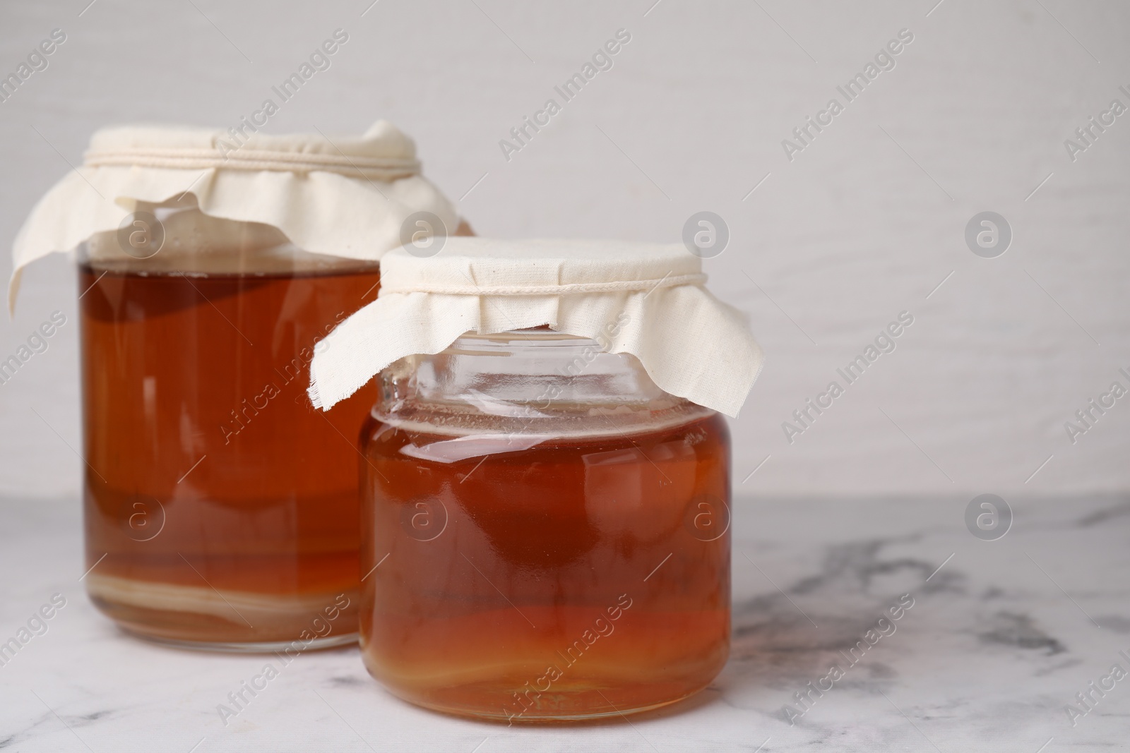 Photo of Tasty kombucha in glass jars on white marble table, space for text