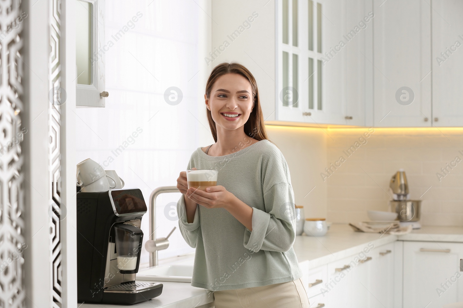 Photo of Young woman enjoying fresh aromatic coffee near modern machine in kitchen
