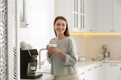 Young woman enjoying fresh aromatic coffee near modern machine in kitchen