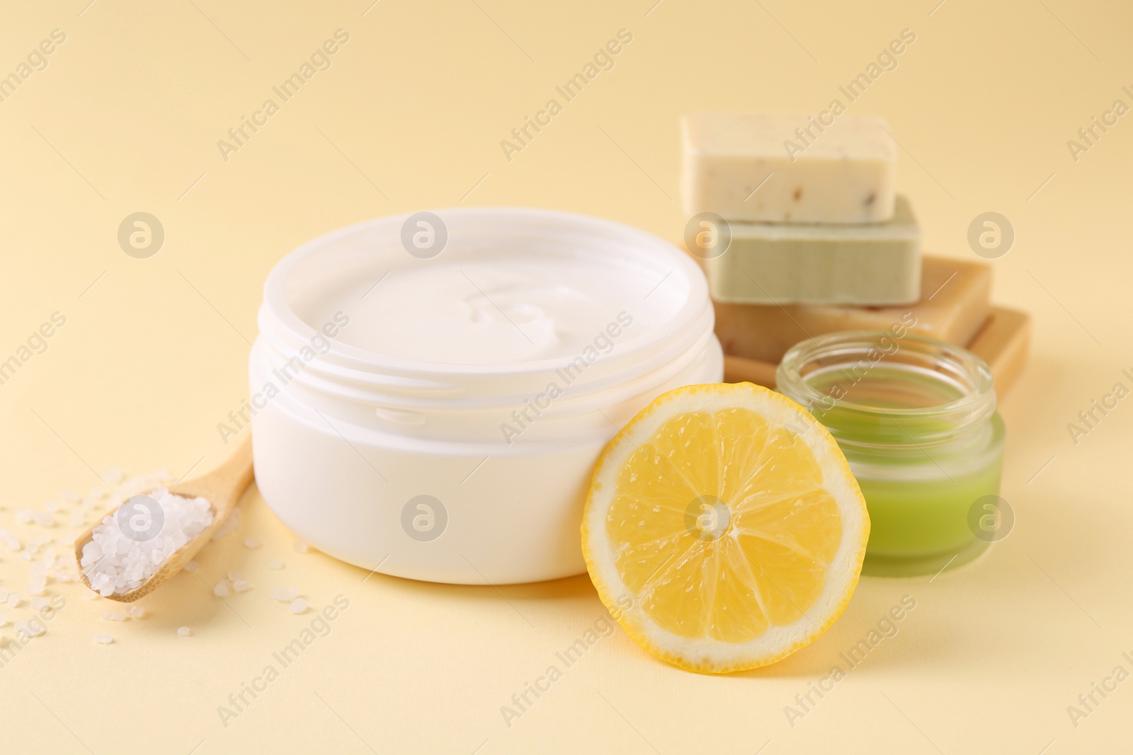 Photo of Moisturizing cream in open jars, soap bars, sea salt and lemon on beige background. Body care products