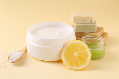 Photo of Moisturizing cream in open jars, soap bars, sea salt and lemon on beige background. Body care products