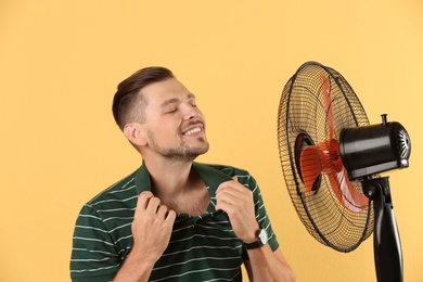 Man refreshing from heat in front of fan on color background