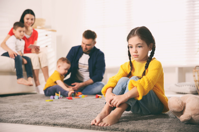 Unhappy little girl feeling jealous while parents spending time with other children at home