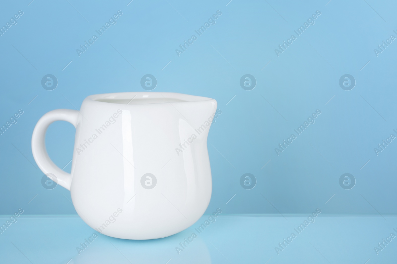 Photo of Jug of fresh milk on light blue background, space for text