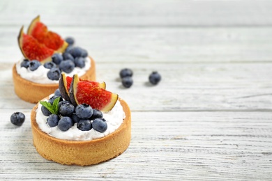 Photo of Tarts with blueberries and figs on white wooden table, space for text. Delicious pastries