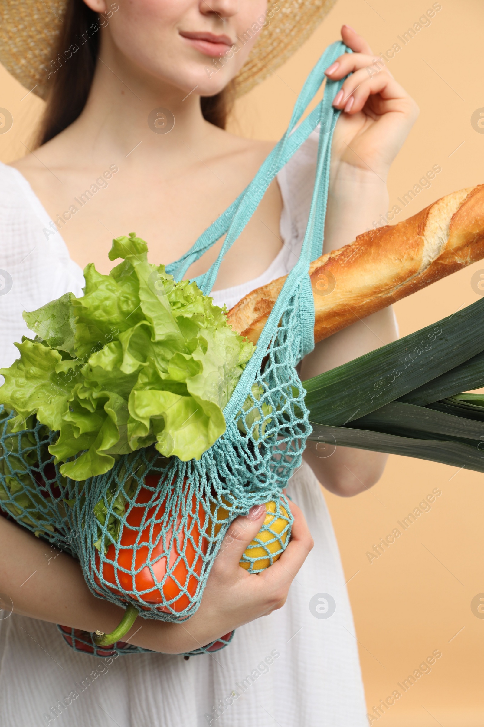 Photo of Woman with string bag of fresh vegetables and baguette on beige background, closeup