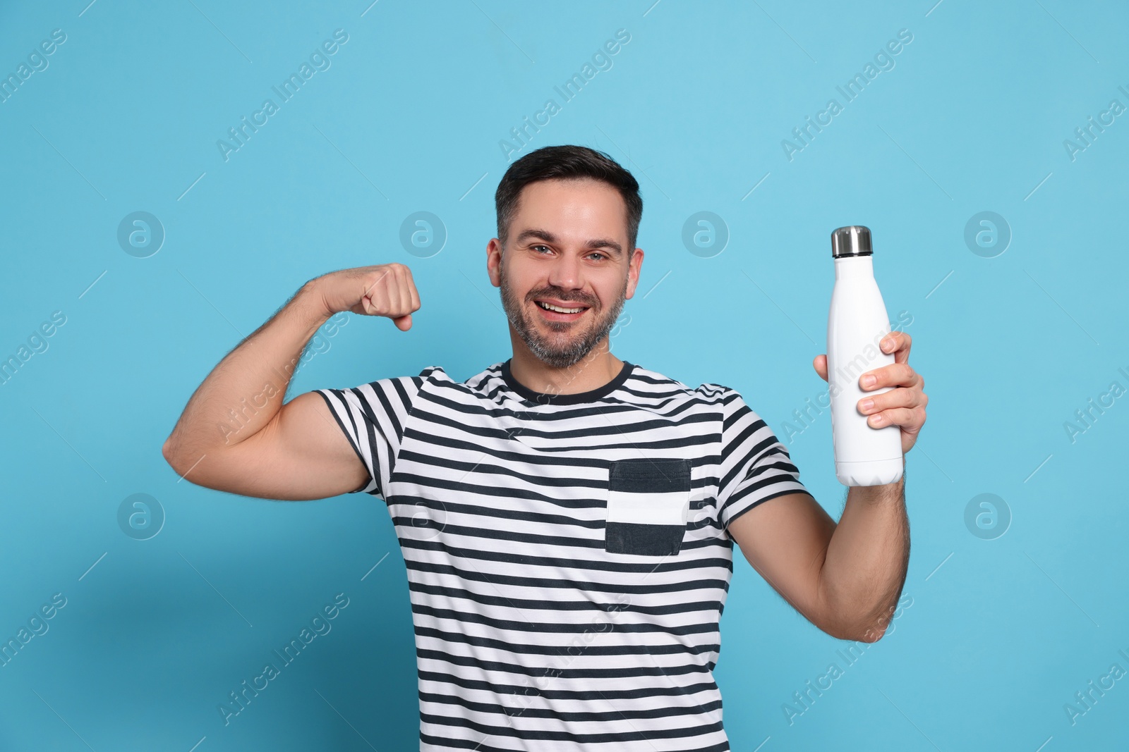 Photo of Happy man holding thermo bottle and showing arm on light blue background