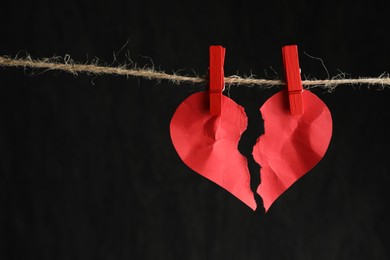Photo of Halves of torn red paper heart on rope against black background, space for text Broken heart
