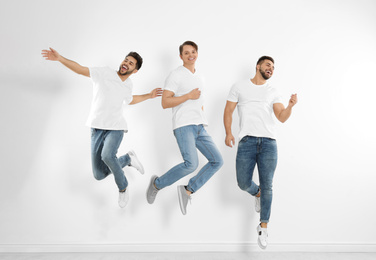 Group of young men in stylish jeans jumping near white wall