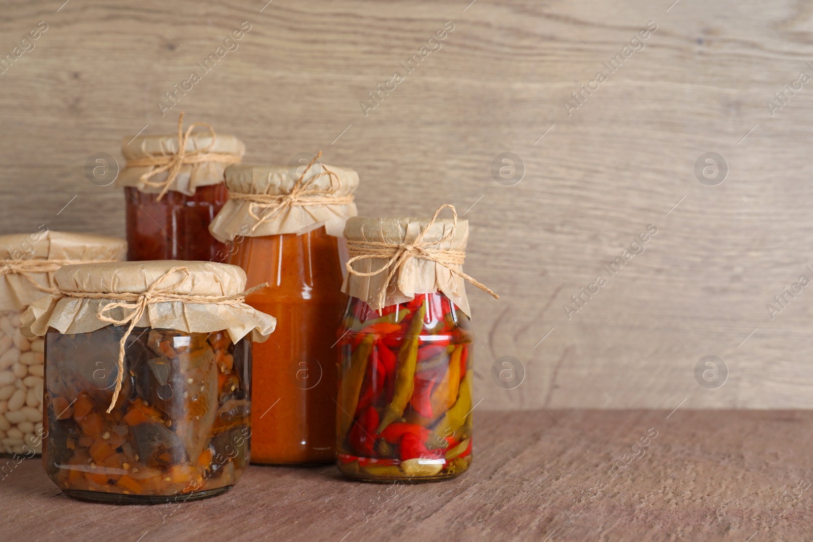 Photo of Jars of tasty pickled vegetables on brown table. Space for text