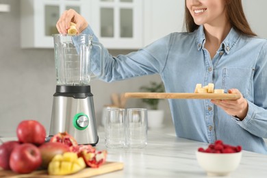 Photo of Beautiful young woman adding banana into blender for tasty smoothie in kitchen, closeup