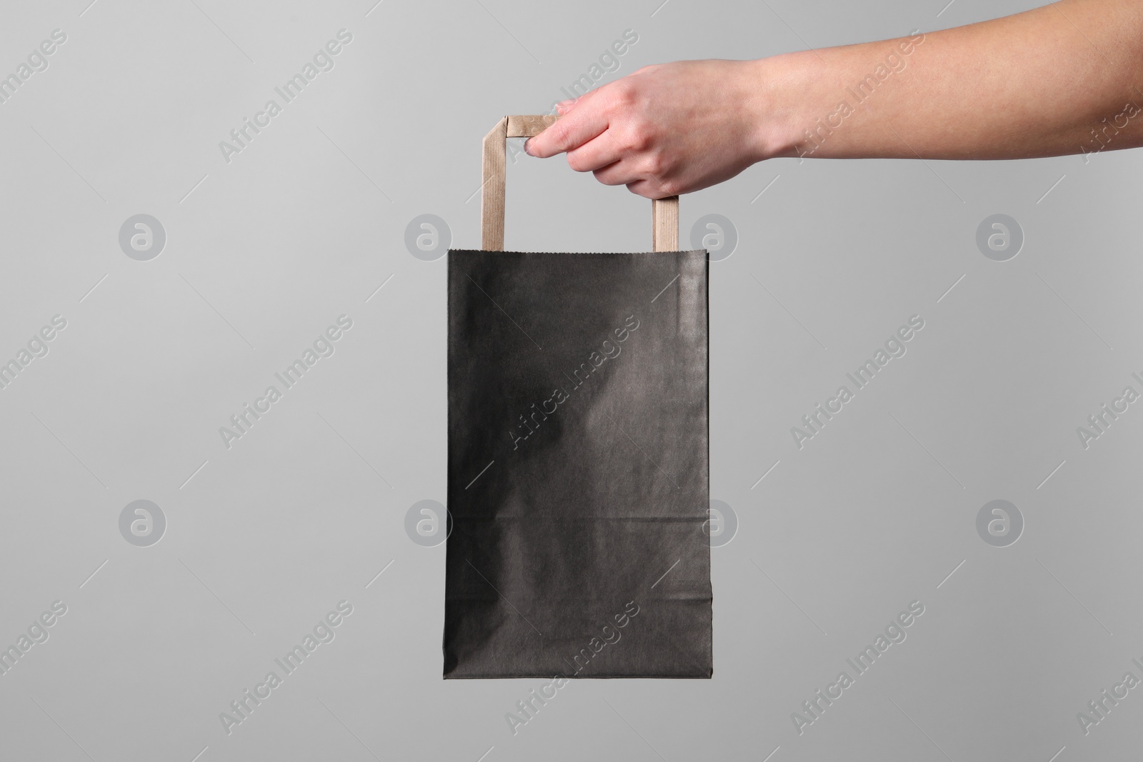 Photo of Woman holding paper shopping bag on grey background, closeup